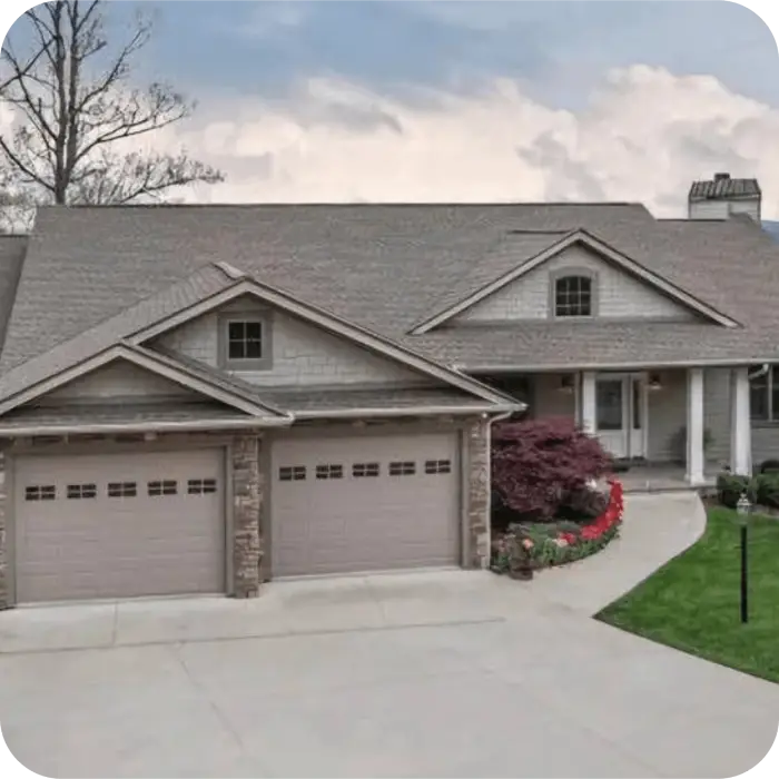 A suburban house with a large driveway leading up to a three-car garage. The house has a stone and siding exterior with a gable roof.