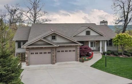 The house has a gray exterior with a matching gray roof. It's got a bit of a rustic touch with stone accents on the garage pillars